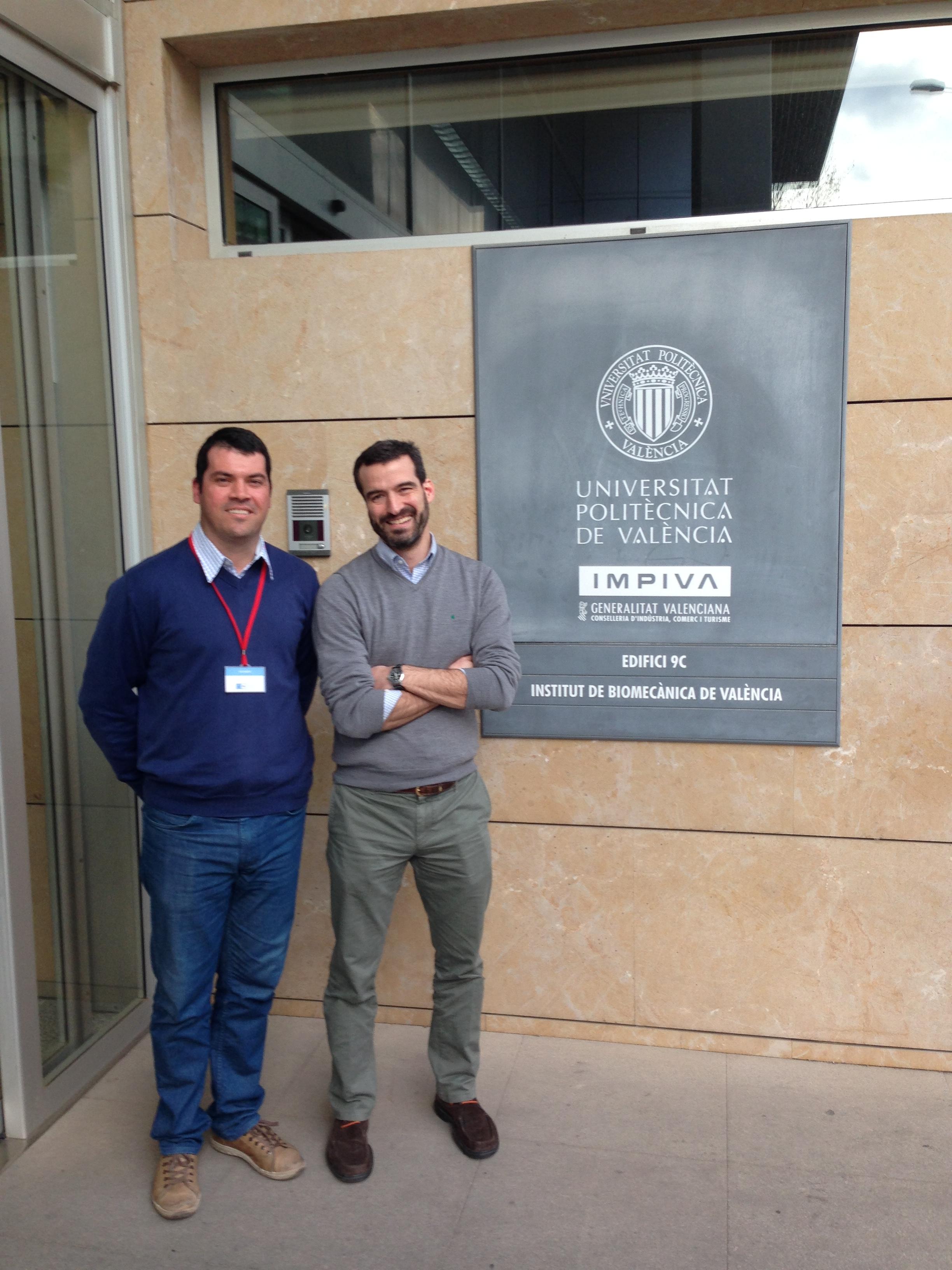 dois homens, o da esquerda sendo o professor Felipe carpes, posam para a foto ao lado de placa do Instituto de biomecânica de Valência