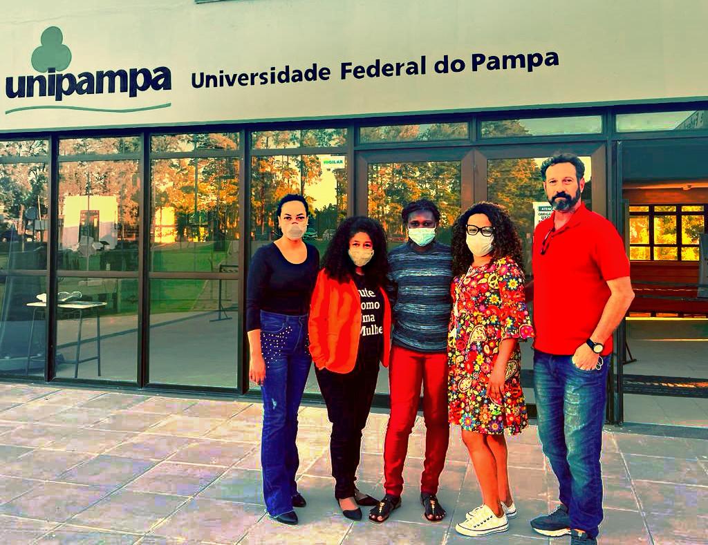 Foto colorida com a estudante Cesaltina ao centro, ao lado de equipe de recepção, ao fundo entrada do Campus Caçapava do Sul