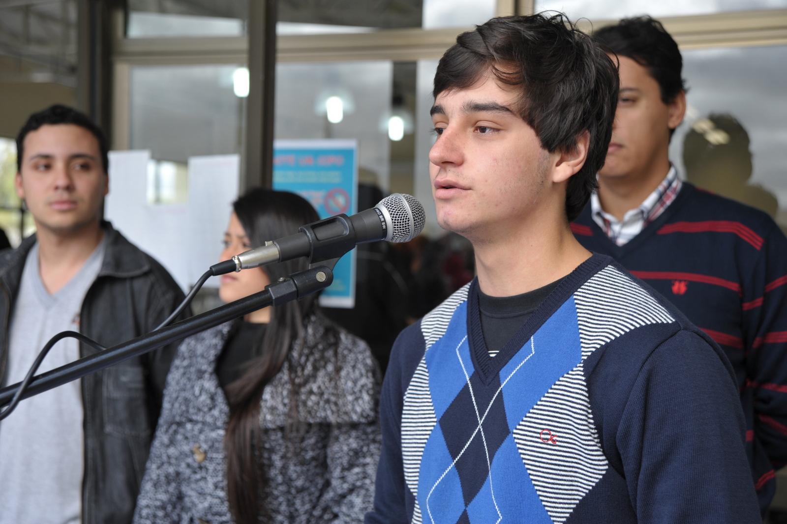 O aluno Angélico Xavier está em pé, à direita na foto e fala ao microfone