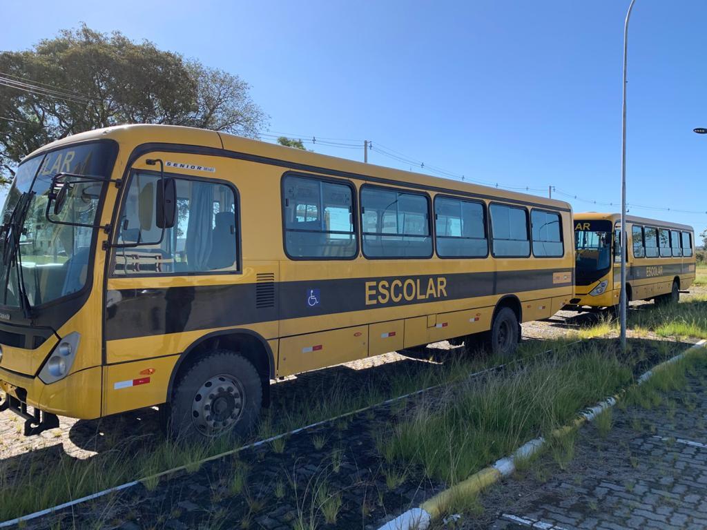 no estacionamento a ceu aberto, os dois ônibus amarelo com faixa preta na lateral e a palavra escolar em amarelo
