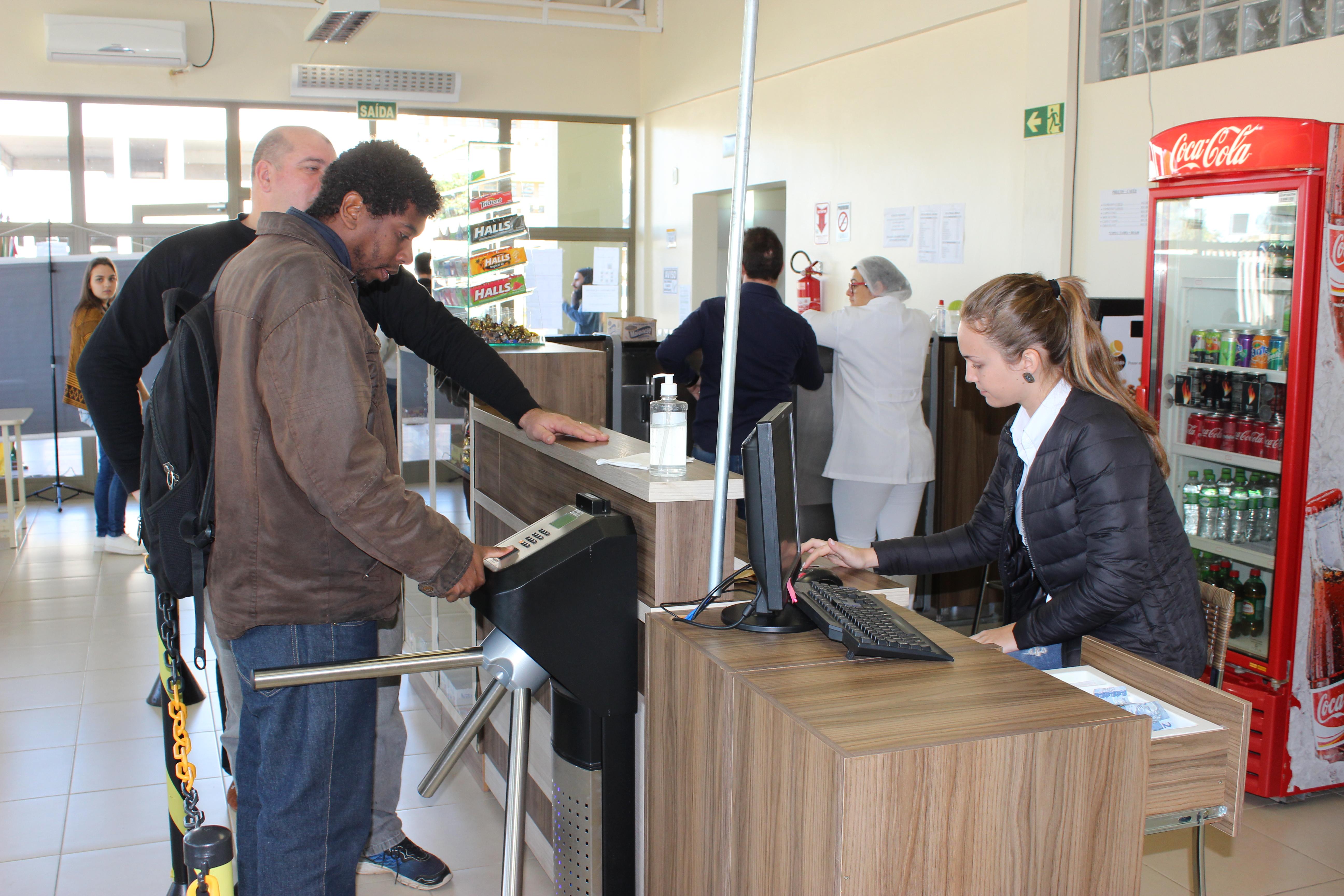 Pessoas fazendo pagamento no caixa do RU e passando pela catraca de identificação biométrica. 