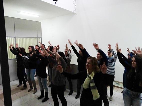 pessoas estão dentro de uma sala e realizam movimentos de dança, com os braços levantados.
