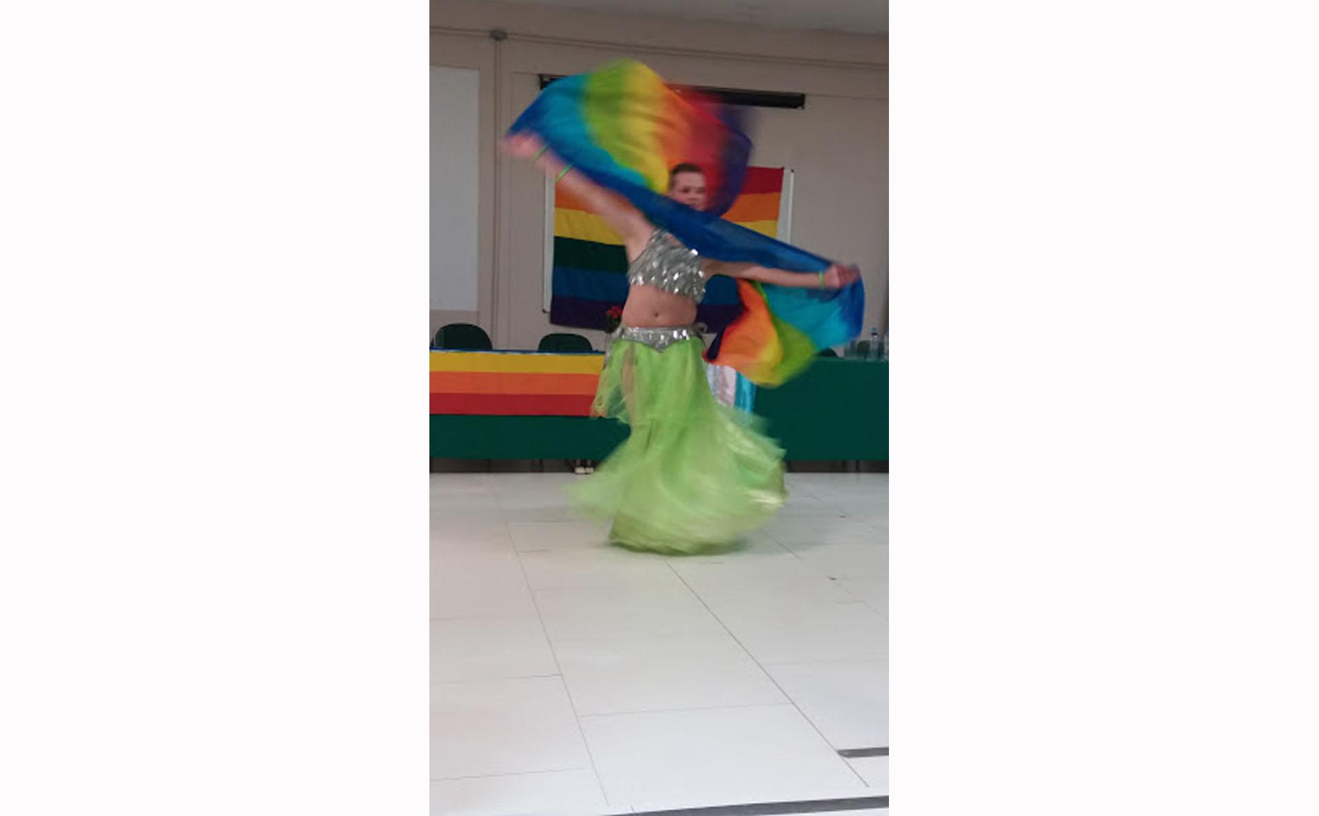 Bailarino apresenta coreografia de dança do ventre em frente à bandeira LGBTQ+