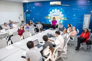 Atividade de compartilhamento de conhecimentos com docentes da UCB. mulher branca palestrando em pé para diversas pessoas sentadas em uma mesa em lugar fechado