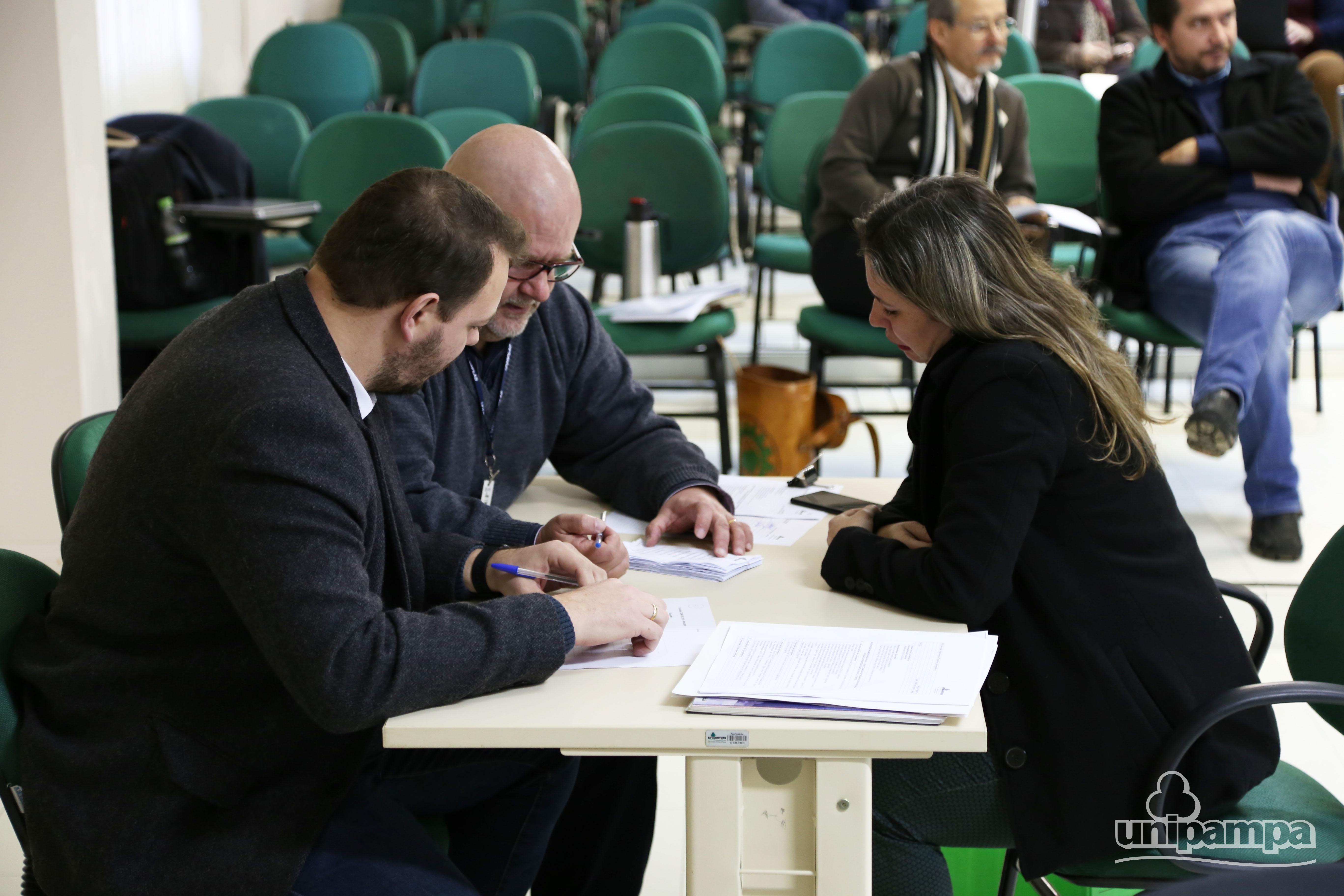 na foto, três pessoas fazem a contagem dos votos ao Concur durante a reunião do Consuni