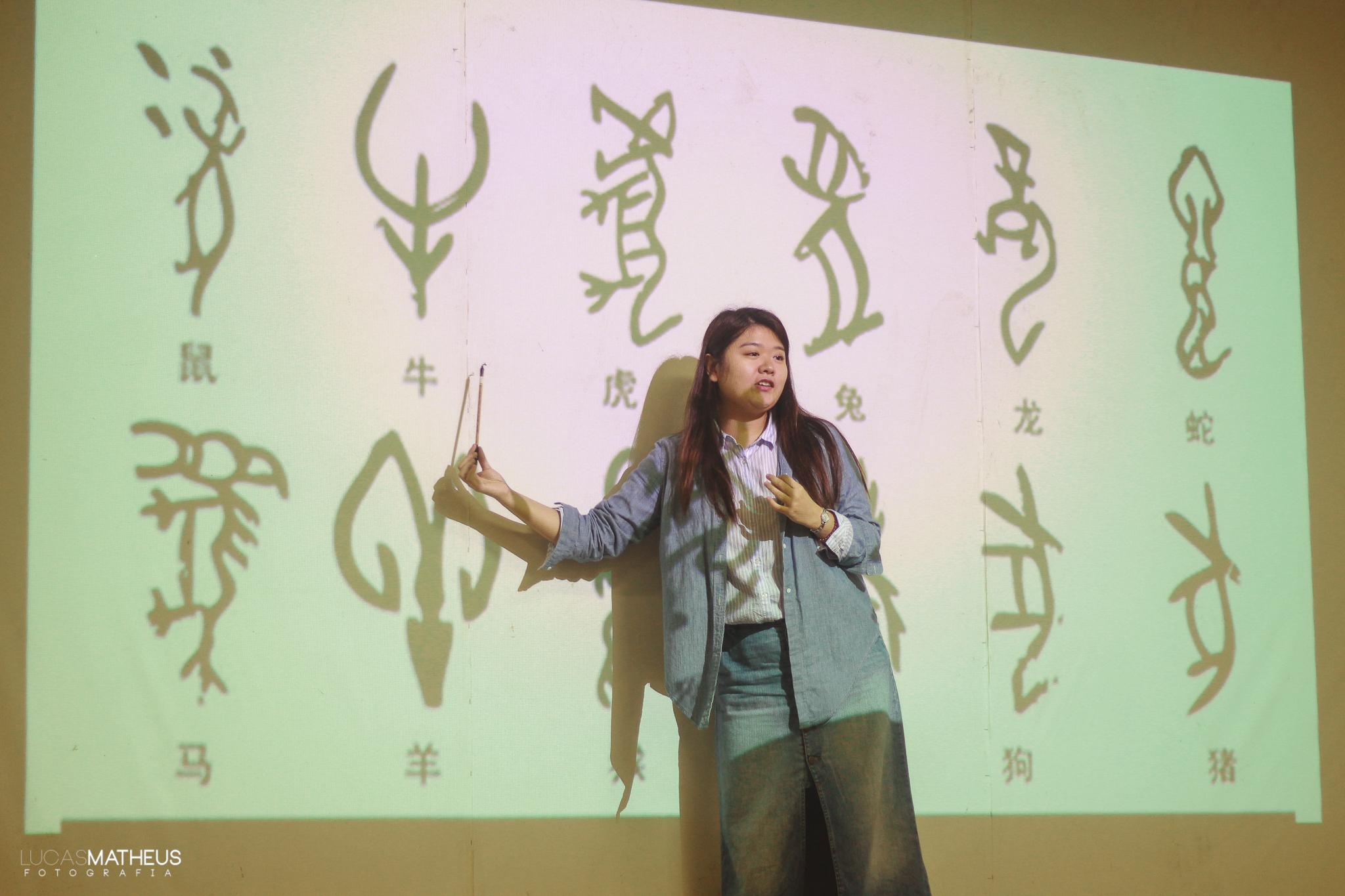 Na imagem uma das professoras palestrantes apresenta símbolos chineses com uma projeção na parede. 