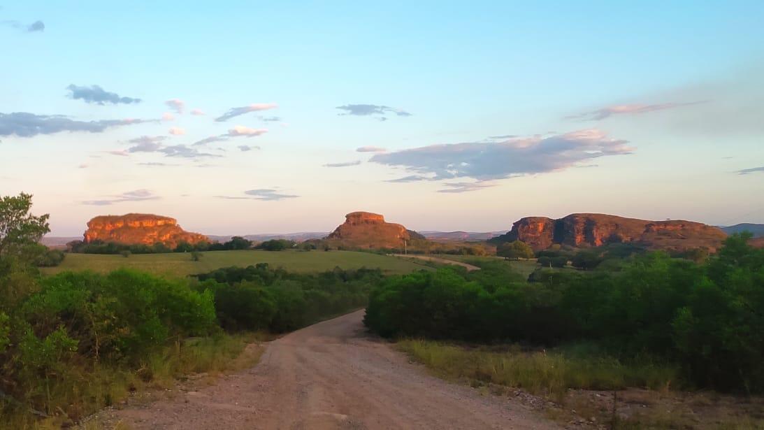 Panorama de três grandes rochas no horizonte acima de uma estrada de terra.